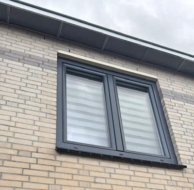 Detail van een antracietgrijs draai-kiepraam in een lichte steenmuur